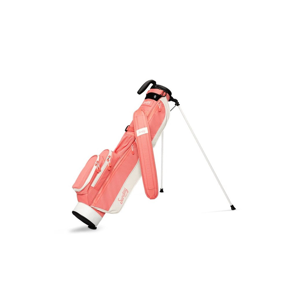 A pink and white golf bag with a stand mechanism, featuring multiple pockets and a shoulder strap with a support stand being used.