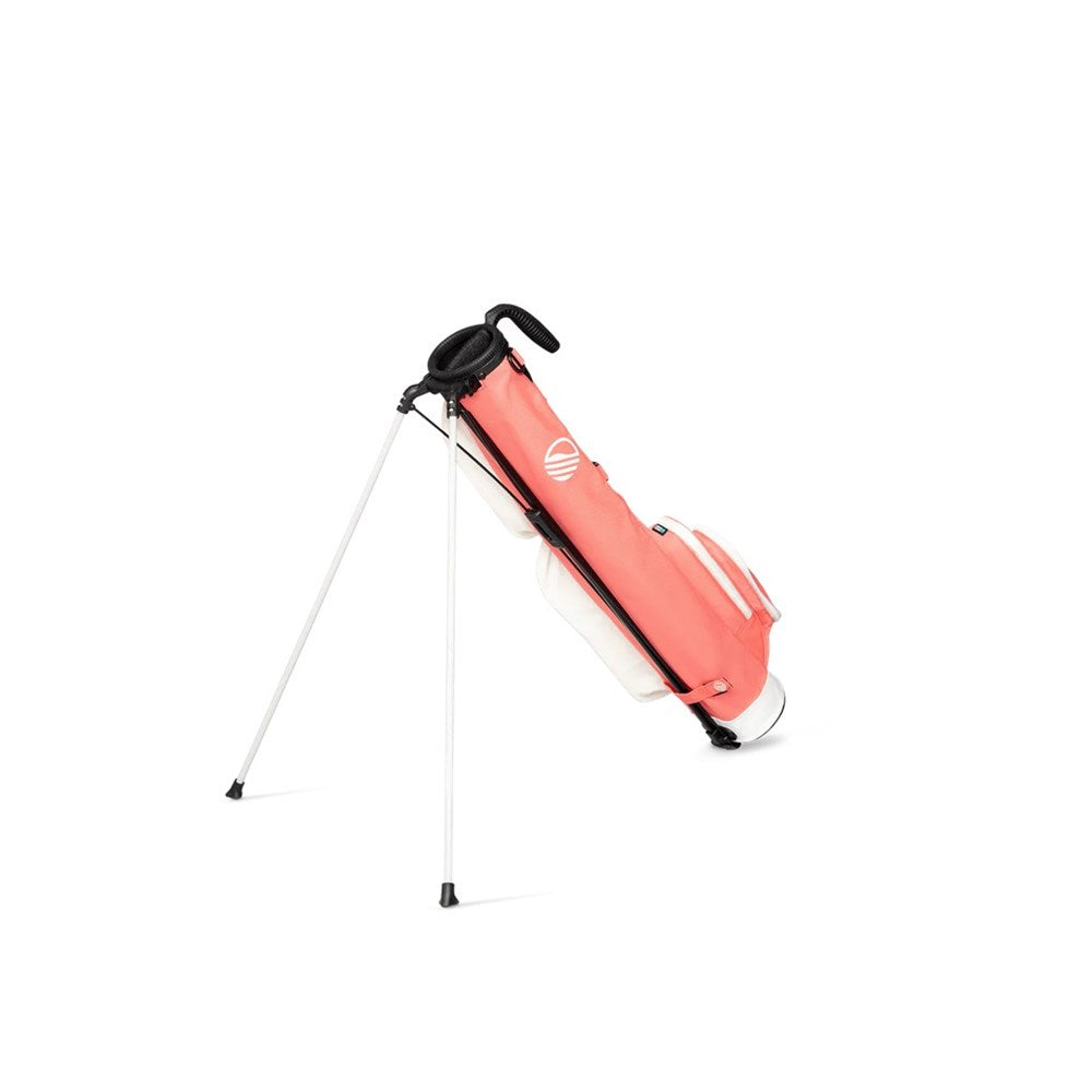 A pink and white golf bag with a stand mechanism, featuring multiple pockets and a shoulder strap with a support stand being used.